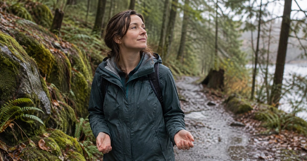 An adult woman pausing on a woodland walk after light rain